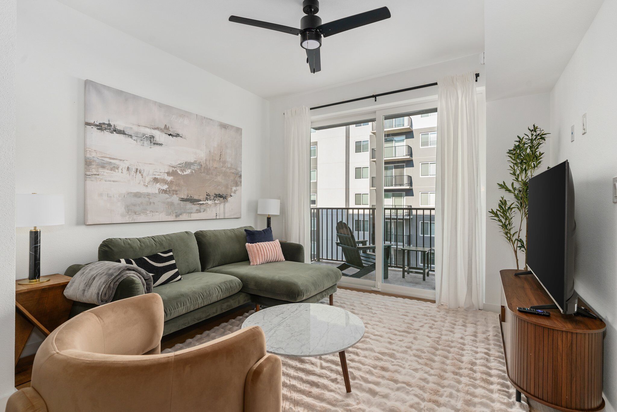 A modern living room with a green sofa, a beige armchair, a round coffee table, and a flat-screen TV on a wooden stand.