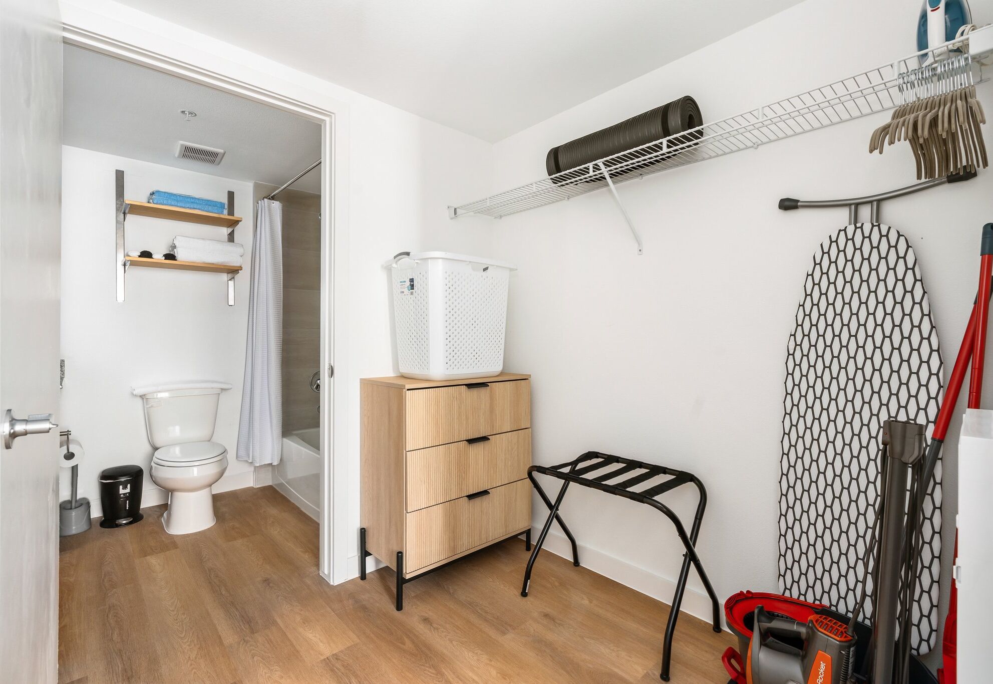 Une petite salle de bain comprenant des toilettes, un meuble en bois, un étendoir et un porte-linge fixé au mur.