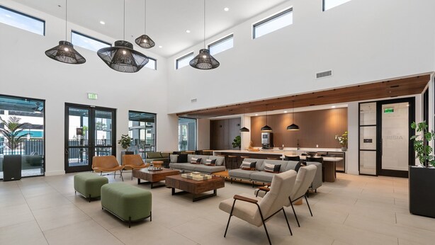 Un'ampia hall con una moderna zona salotto, pouf verdi e lampade pendenti.