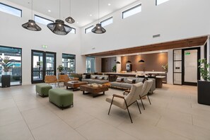 A spacious lobby with a modern sofa set, green ottomans, and hanging pendant lights. - Lodgeur Energy Corridor (Houston)