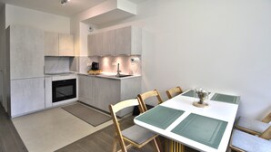 Une cuisine moderne dotée d’un four encastré, d’une table à manger avec des chaises et d’un petit îlot central avec un évier.