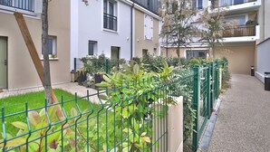 Un immeuble résidentiel doté de nombreux balcons, d’une clôture verdoyante et d’un petit jardin.
