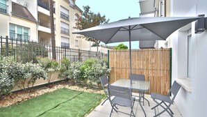 Une terrasse avec une table et des chaises, une clôture en bois et une zone herbeuse.