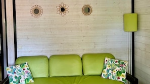 Un canapé vert agrémenté de coussins à motifs floraux, un mur en bois orné de trois miroirs décoratifs et une lampe verte.