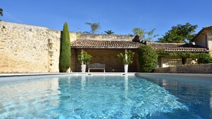 A swimming pool with clear water, surrounded by stone walls and a building with a tiled roof.