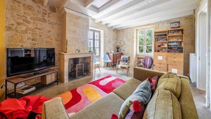 A cozy living room with a stone wall, a fireplace, a television, and a bookshelf.