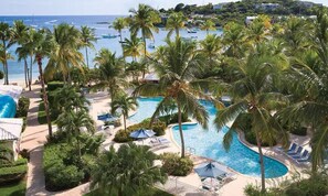 A resort with a large swimming pool surrounded by palm trees, a beach, and boats in the background. - Bayside Retreat - Walk to Cowpet Beach, Pool w/ Grotto, Oceanview! (St Thomas)