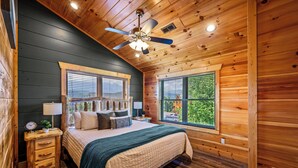 Une chambre à coucher dans un chalet en bois, avec un lit, des tables de chevet, un ventilateur de plafond et des fenêtres équipées de stores.