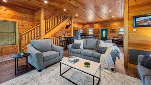 Un intérieur de chalet chaleureux avec deux canapés gris, une petite table basse et un escalier menant à une mezzanine.