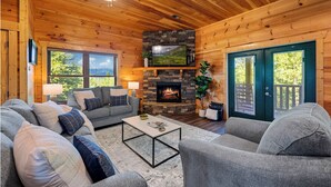 L’intérieur d’un chalet accueillant, avec une cheminée en pierre, des murs en bois et une grande fenêtre.
