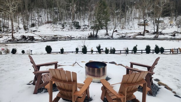 Een besneeuwde buitenruimte met twee Adirondack-stoelen en een metalen vuurkorf.