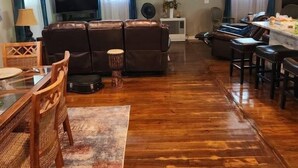 Een ruime woonkamer met een houten plafond, een grote bank, een eettafel met stoelen en een televisie.