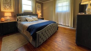 Een slaapkamer met een groot bed, twee nachtkastjes met lampen, een dressoir en een plafondlamp.