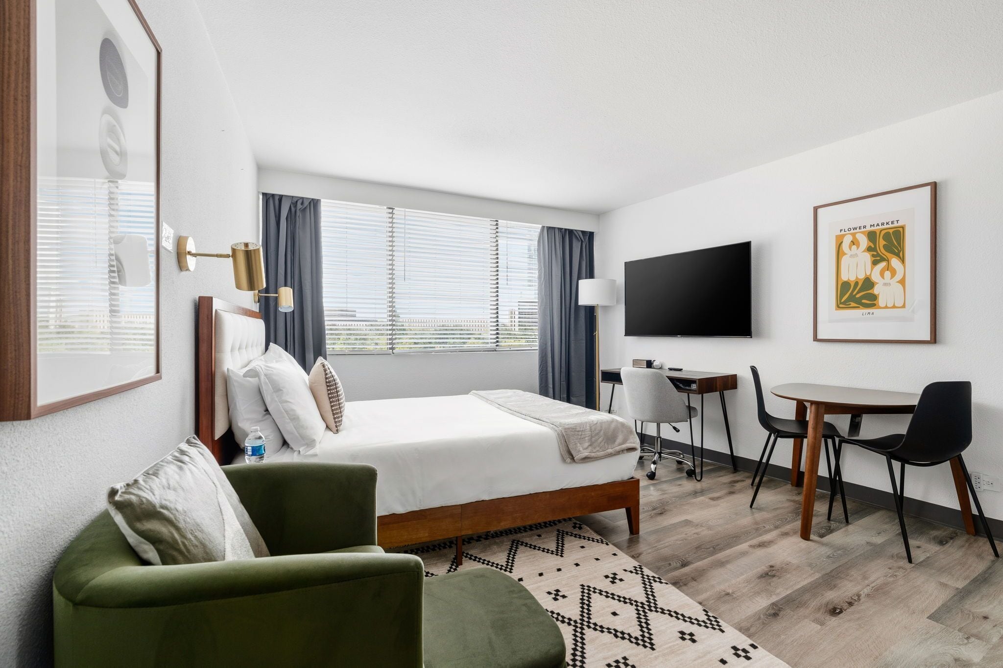 A hotel room with a bed, a desk, a chair, a television, and a framed picture on the wall.
