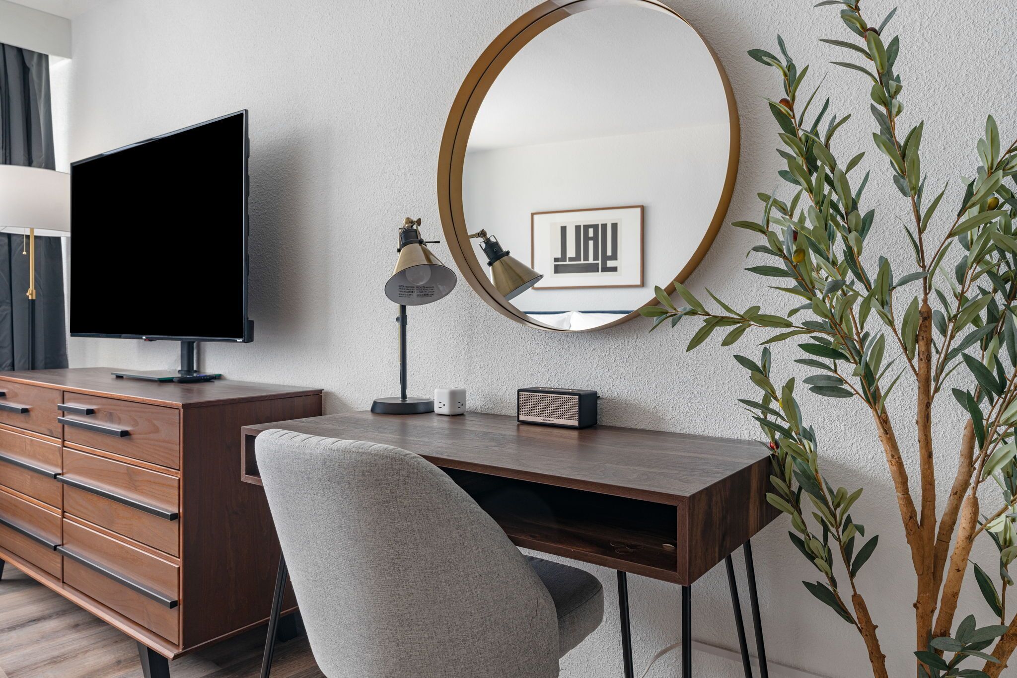 A modern office space with a desk, chair, television, lamp, and a large mirror.