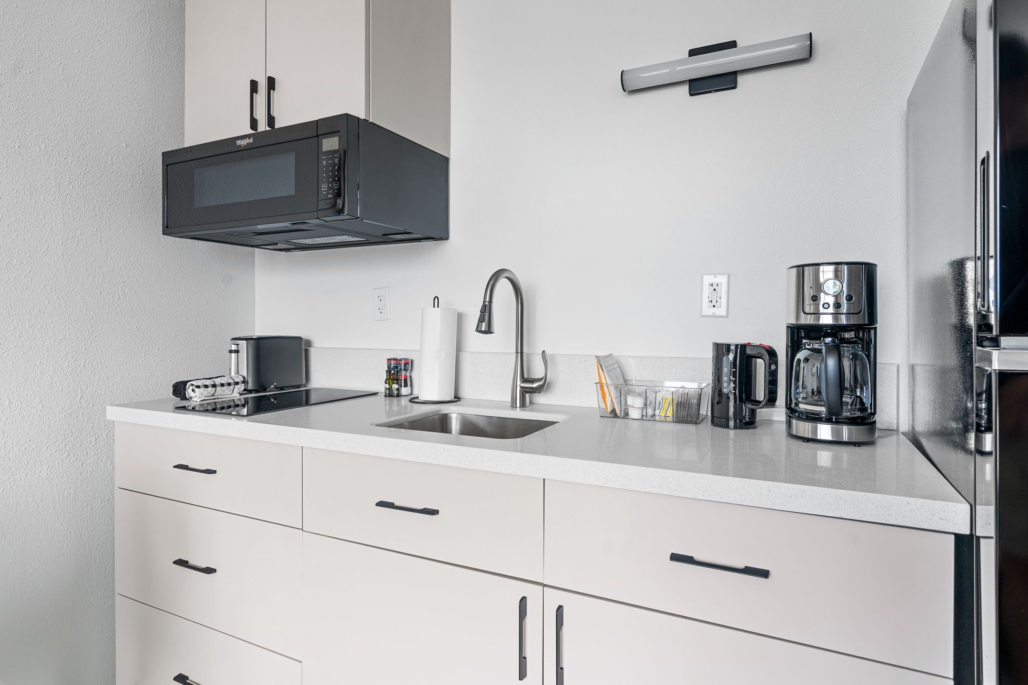 A modern kitchen with white cabinets, a black microwave, a stainless steel sink, and a coffee maker.