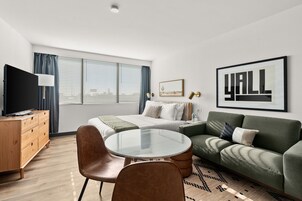 A modern hotel room with a bed, a green sofa, a round glass table, and a TV.