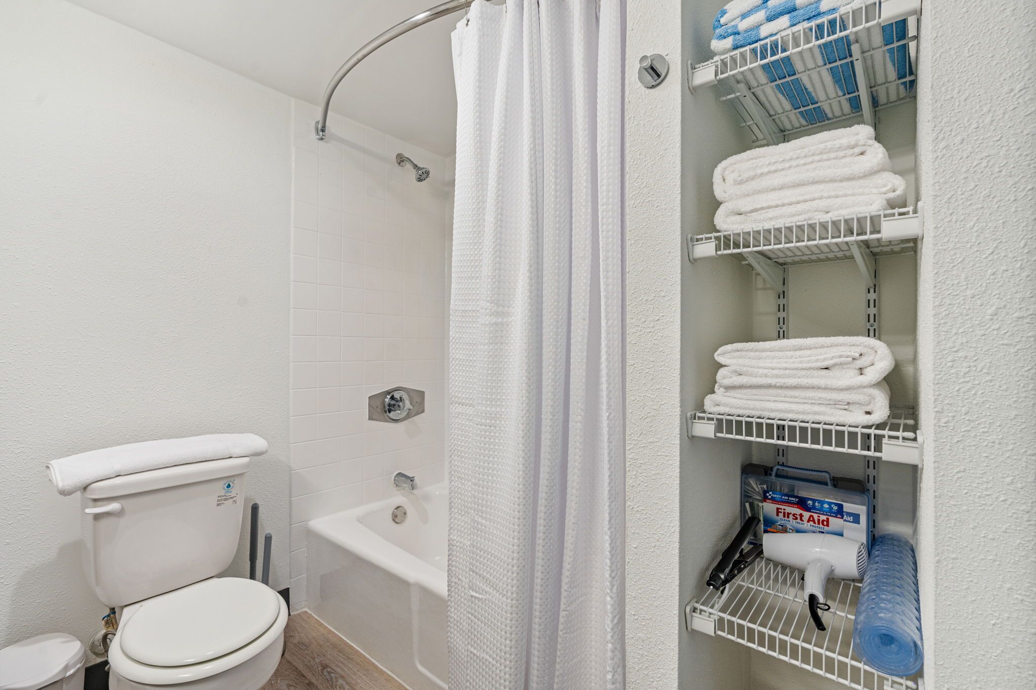 A bathroom with a toilet, shower, and shelves with towels and toiletries.
