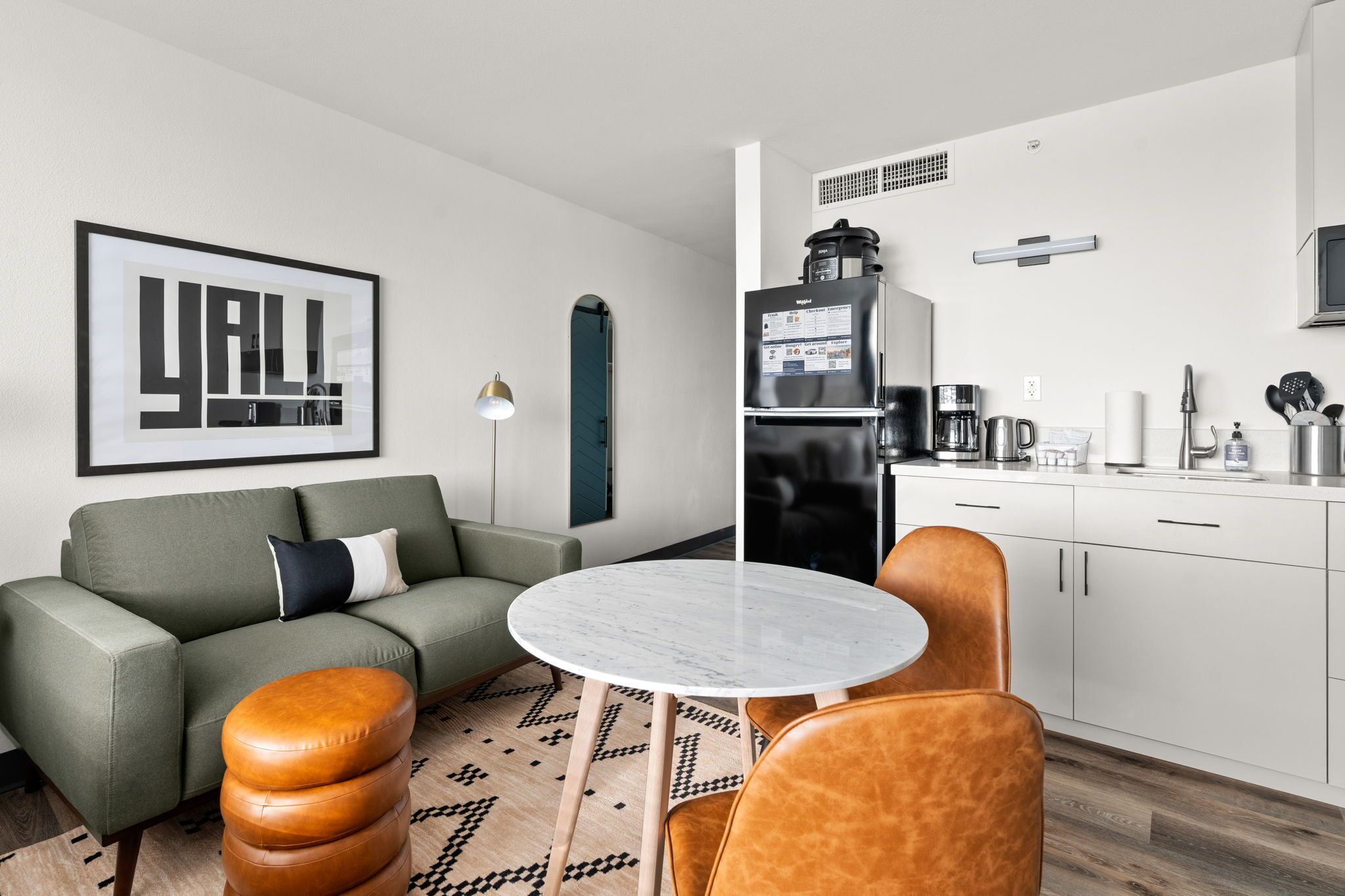 A modern living room with a green sofa, a round marble table, and a coffee machine.