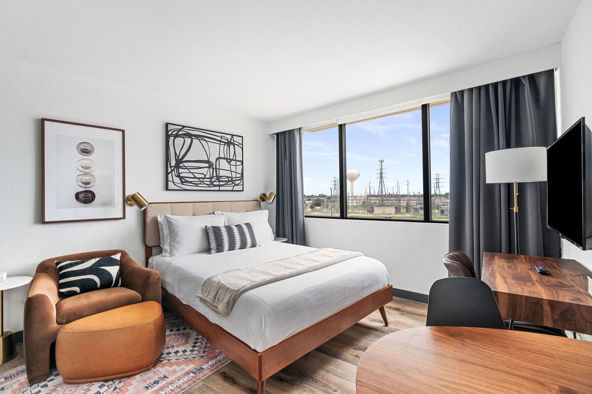 A modern hotel room with a large bed, a desk, a chair, and a TV.