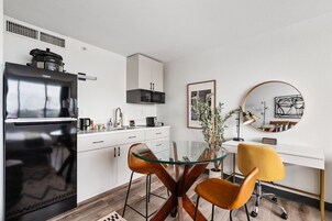 A modern kitchen with a black refrigerator, white cabinets, and a glass dining table with two chairs.