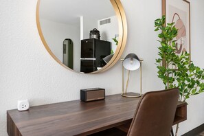 A modern room with a wooden desk, a round mirror, a small speaker, a floor lamp, and a potted plant. - Lodgeur Upper Kirby (Houston)