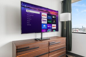 A flat-screen TV mounted on a wall displaying a streaming service interface with various options. - Lodgeur Upper Kirby (Houston)