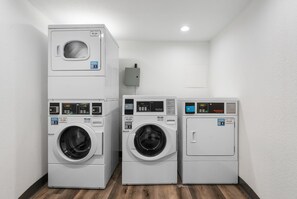 A laundry room with four stacked washing machines, a control panel, and a wall-mounted electrical box. - Lodgeur Upper Kirby (Houston)