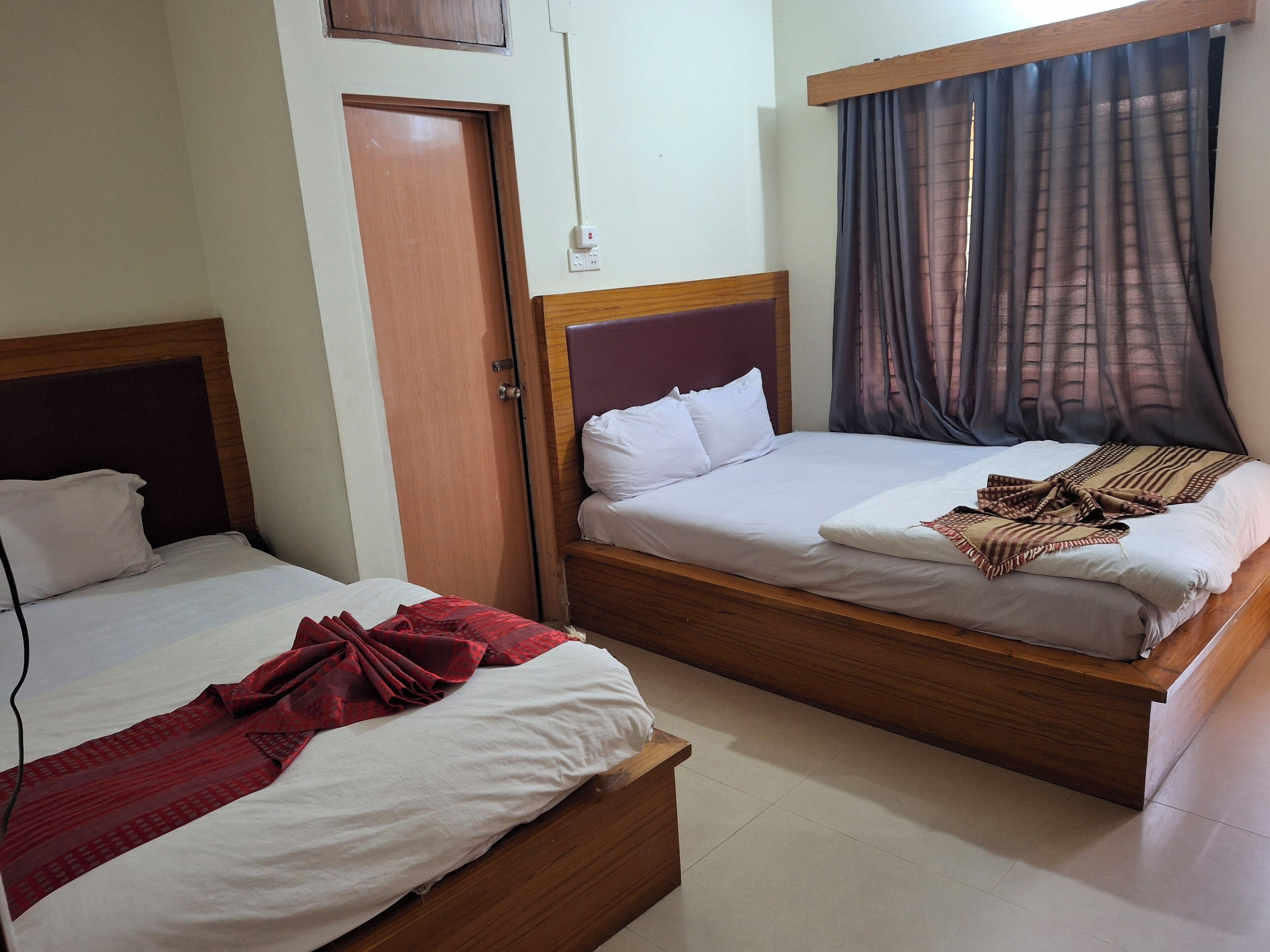 A hotel room with two wooden beds, a red blanket on one bed, and a patterned blanket on the other.