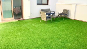 A patio with artificial grass, wicker furniture, and a sliding glass door leading to a room.