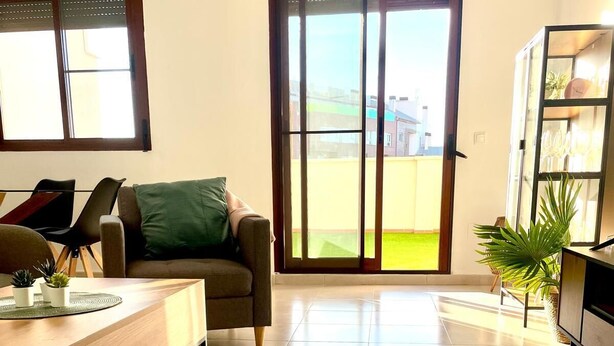 A spacious living area with a sofa, a dining table, and a sliding glass door leading to a balcony.