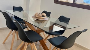 A dining area with a glass table surrounded by six black chairs with wooden legs.