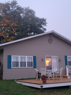 A single-story house with a porch, two windows with blue shutters, and a satellite dish on the roof. - Sunny Dock Rentals LLC- Barefoot Beach Bungalow (Coral)