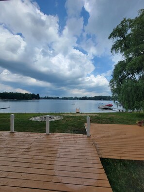 A wooden deck overlooking a lake with boats, a dock, and a weeping willow tree. - Sunny Dock Rentals LLC- Barefoot Beach Bungalow (Coral)