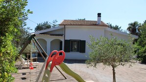 A playground with a seesaw and a small tree in front of a white building with a tiled roof.