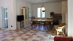 A spacious living area with a dining table, chairs, a television, and a wicker chair.