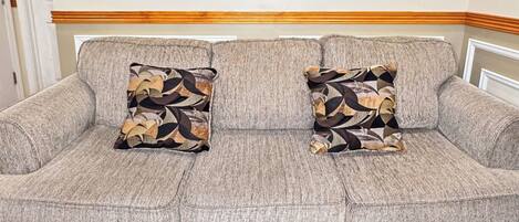Un sofá gris con dos cojines estampados, suelo de madera y una pared con paneles empotrados.