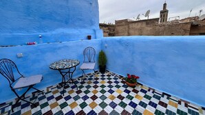 A rooftop terrace with a blue wall, a tiled floor, two chairs, a small table, and a potted plant. - Riad la Mentha (Fès)