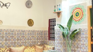 A room with a patterned wall, a sofa, a small table, a potted plant, and a decorative hanging. - Riad la Mentha (Fès)