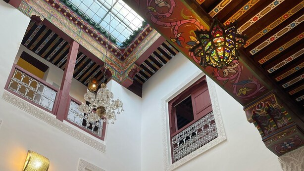 A multi-level interior with ornate ceiling designs, multiple windows with decorative grills, and wall-mounted light fixtures. - Riad la Mentha (Fès)