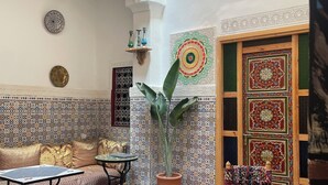 A room with a patterned tile floor, a sofa, a chair, a table, and a decorative wall with intricate designs. - Riad la Mentha (Fès)