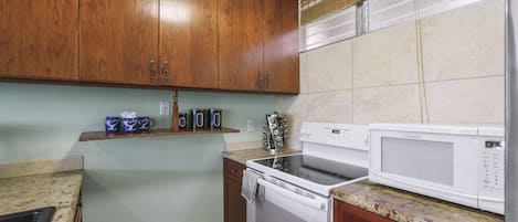 Una cocina con armarios de madera, una estufa, un microondas y un estante con tazas.