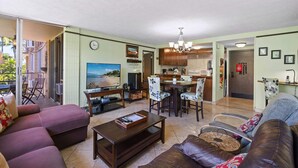 A living room with a television, sofa, and coffee table. There is a kitchen area with a dining table and chairs.
