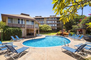A swimming pool with lounge chairs and a building with multiple balconies.