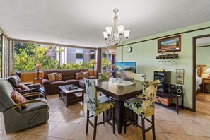 A spacious living room with a sofa, chairs, a dining table, and a view of greenery outside.