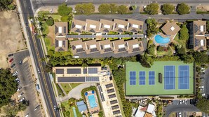 An aerial view of a residential complex with multiple buildings, a swimming pool, tennis courts, and a parking area.