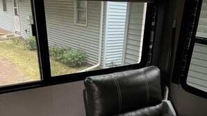 A compact RV interior with a small seating area, a side table, and a window offering a view of a residential area. -  Coleman camper you can pick it up and take it to your favorite campground (Berrien Springs)