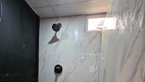 A bathroom with a marble wall, a shower with a glass door, and a tiled floor. - The Studio of Praise - by Zenbreak (Claxton Bay)