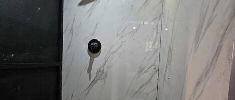 A bathroom with a marble wall, a shower with a glass door, and a tiled floor.