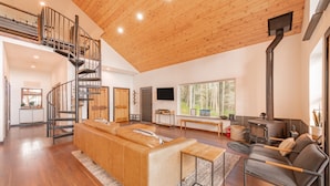 A spacious living area with a wooden ceiling, a built-in fireplace, a sofa, a coffee table, and a TV. - Shotski's Lodge - Secluded Ski-In/Out with Hot Tub, Wildlife and Views (Angel Fire)